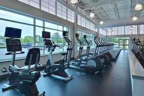 Ein Fitnessstudio mit Cardiogeräten, großen Fenstern und Blick auf parkende Autos vor der Tür.