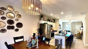 A dining area with a wooden table and chairs, a chandelier, and a kitchen in the background. - Sparkle City Vibes await for you to relax and enjoy! (Spartanburg)