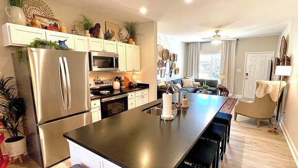 A modern kitchen with stainless steel appliances, a central island, and a dining area with bar stools. - Sparkle City Vibes await for you to relax and enjoy! (Spartanburg)