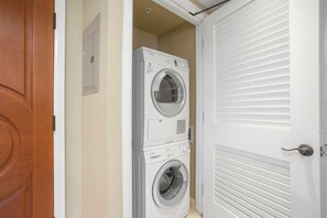 A laundry room with stacked washers and dryers, a wooden door, and a white door with horizontal blinds. - KBM Resorts | 4 FREE CARS | Honua Kai Hokulani | Ocean view | 6-Bedroom Multi-Unit Listing  Recently Remodeled! HK ML-2891 (Lahaina)