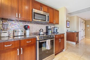 A kitchen with wooden cabinets, a microwave, a stove, and a coffee maker. - KBM Resorts | 4 FREE CARS | Honua Kai Hokulani | Ocean view | 6-Bedroom Multi-Unit Listing  Recently Remodeled! HK ML-2891 (Lahaina)