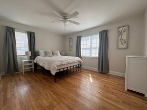 Ein Schlafzimmer mit Bett, Deckenventilator, Nachttisch, Lampe und Heizkörper.