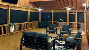 A wooden deck with outdoor seating, ceiling fans, and a TV mounted on the wall. - Lakefront Private Beach, Fire pit, Mile long lake views, Mega Screened in Porch (Ridgeway)
