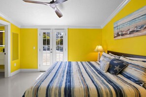 Una camera da letto con un letto, una ventola a soffitto, una porta che dà sull'esterno e un quadro appeso al muro.
