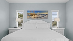 Een slaapkamer met een bed, twee nachtkastjes, twee lampen en een schilderij aan de muur.