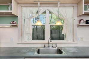 A kitchen with a double sink, a window with lace curtains, and pendant lights. - Silver House | 2/2, Pet Friendly w/ fee (Fredericksburg)
