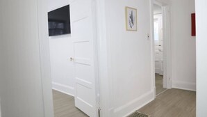 A hallway with white walls, a door, and a vent on the floor.