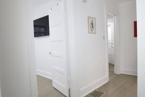 A hallway with white walls, a door, and a vent on the floor.
