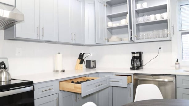 A modern kitchen with grey cabinets, a built-in wine rack, a kettle, a coffee maker, and a dishwasher.