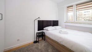 Un dormitorio con cama, mesita de noche, lámpara y ventana.