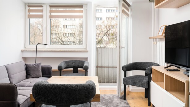 Una sala de estar moderna con un sofá, dos sillones, una mesa de madera, un televisor y una ventana con persianas.