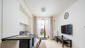 Ett modernt vardagsrum med en tv, en matplats med bord och stolar samt utsikt genom en glasdörr till en balkong.