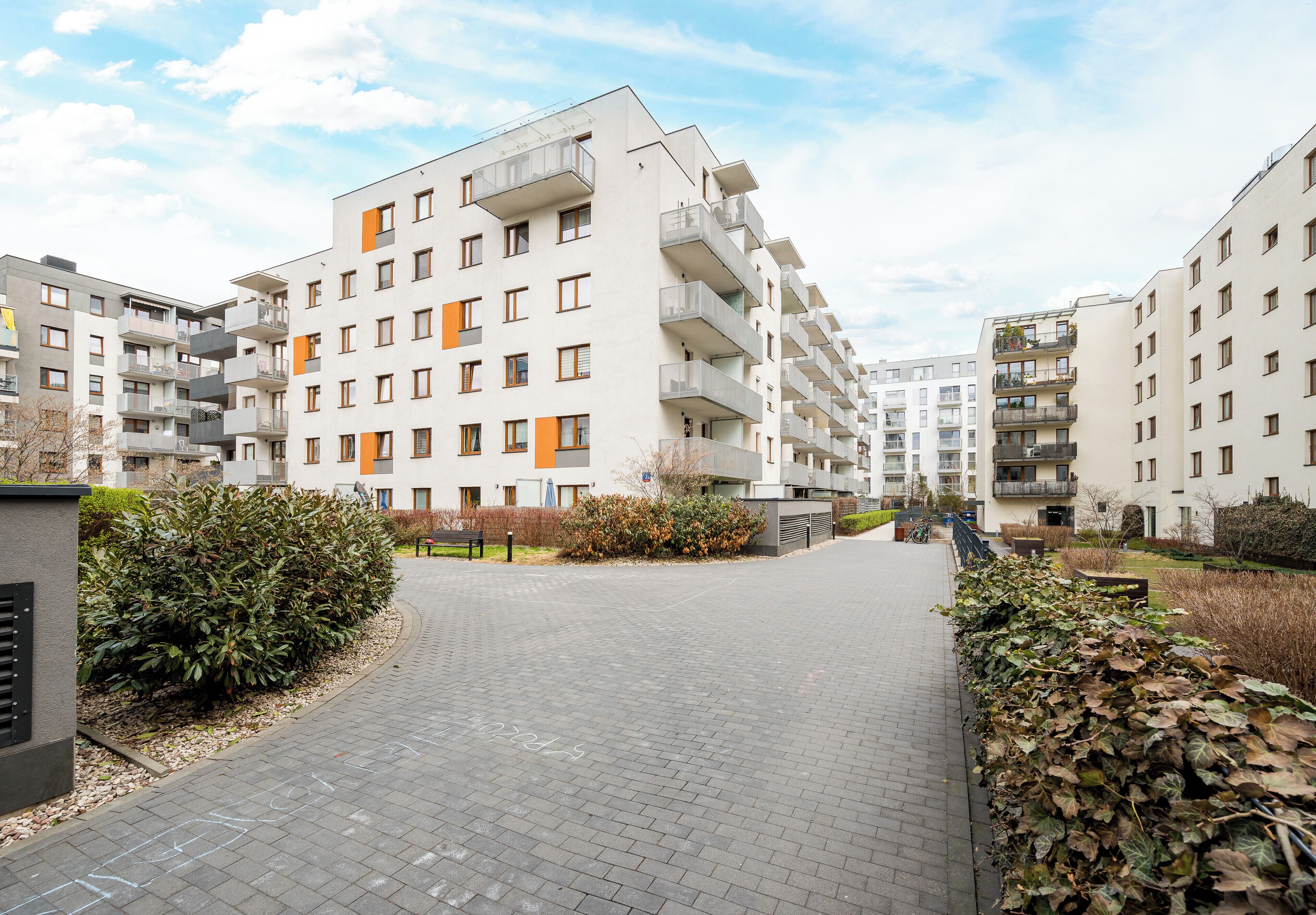 Ein mehrstöckiges Wohngebäude mit Balkonen, einem gepflasterten Weg und einer Hecke.