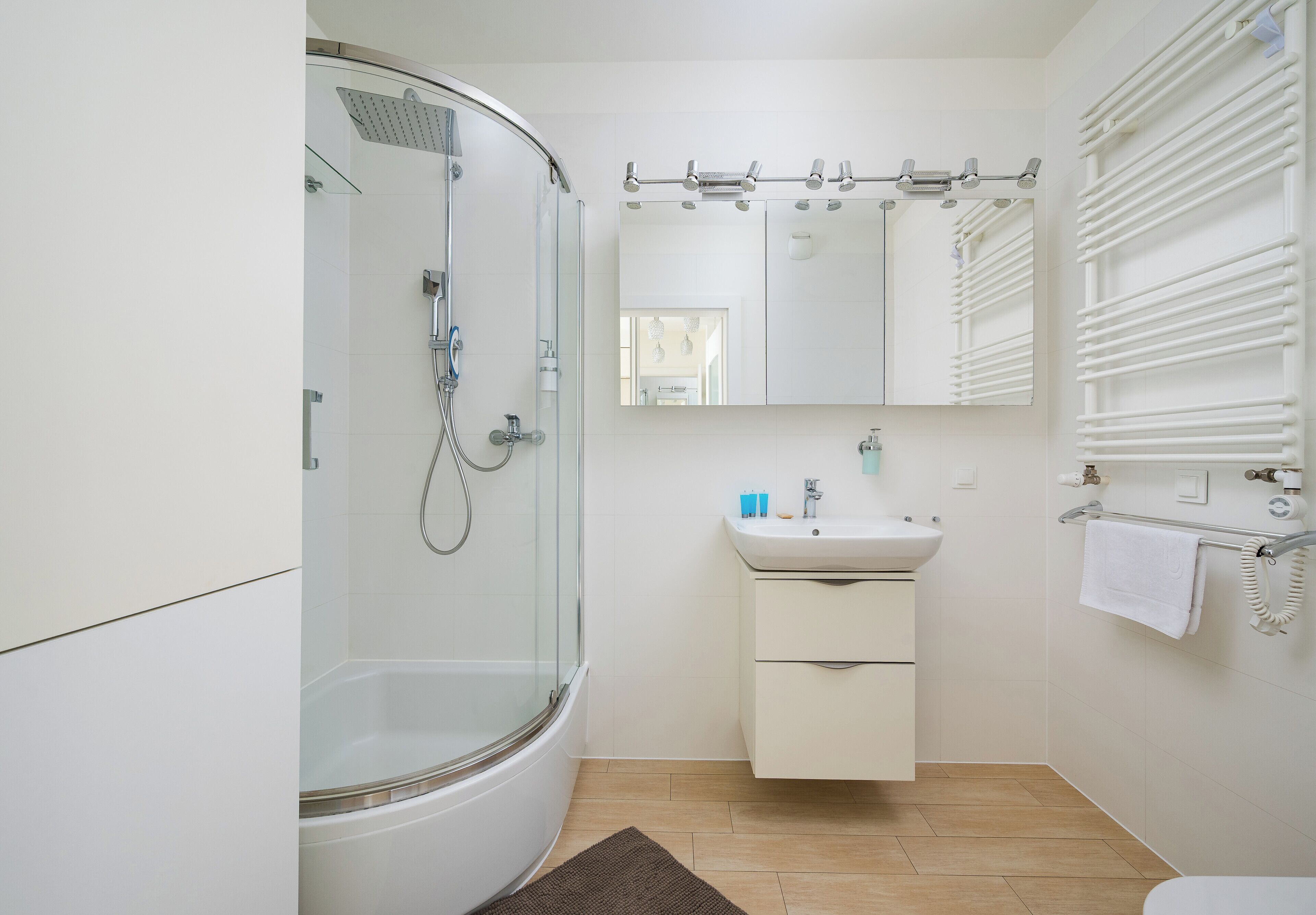 A modern bathroom with a glass-enclosed shower, a white sink with a mirror above, and a towel rack.