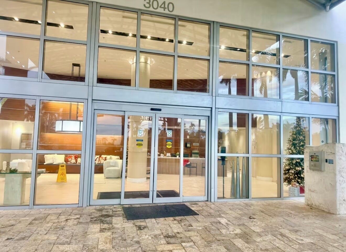 A hotel entrance with a glass facade, a Christmas tree, and a number '3040' above the doors.