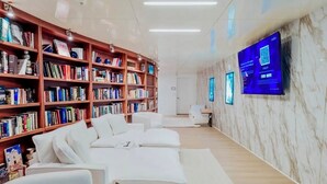 A modern living room with a sofa, white cushions, a bookshelf, and a flat-screen TV mounted on the wall. - Luxury Waterfront Studio Condo with Balcony Views (Fort Myers)