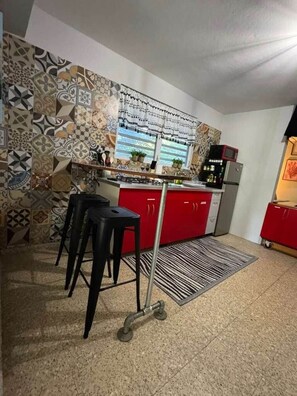 Une cuisine avec des meubles de couleur rouge, un pare-feu décoré et une fenêtre avec des rideaux.