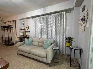 A living room with a sofa, two side tables, a potted plant, a bunk bed, and a wall-mounted shelf.