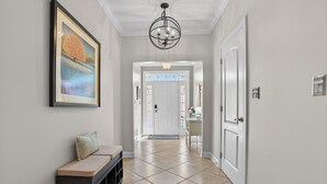 A hallway with a bench, a door, a chandelier, and a framed picture on the wall. - One Level Rehoboth Beach House Steps to Pool (Rehoboth Beach)