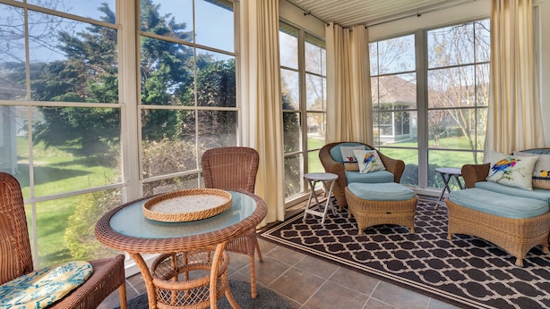 A sunroom with large windows, wicker furniture, and a ceiling fan. - One Level Rehoboth Beach House Steps to Pool (Rehoboth Beach)