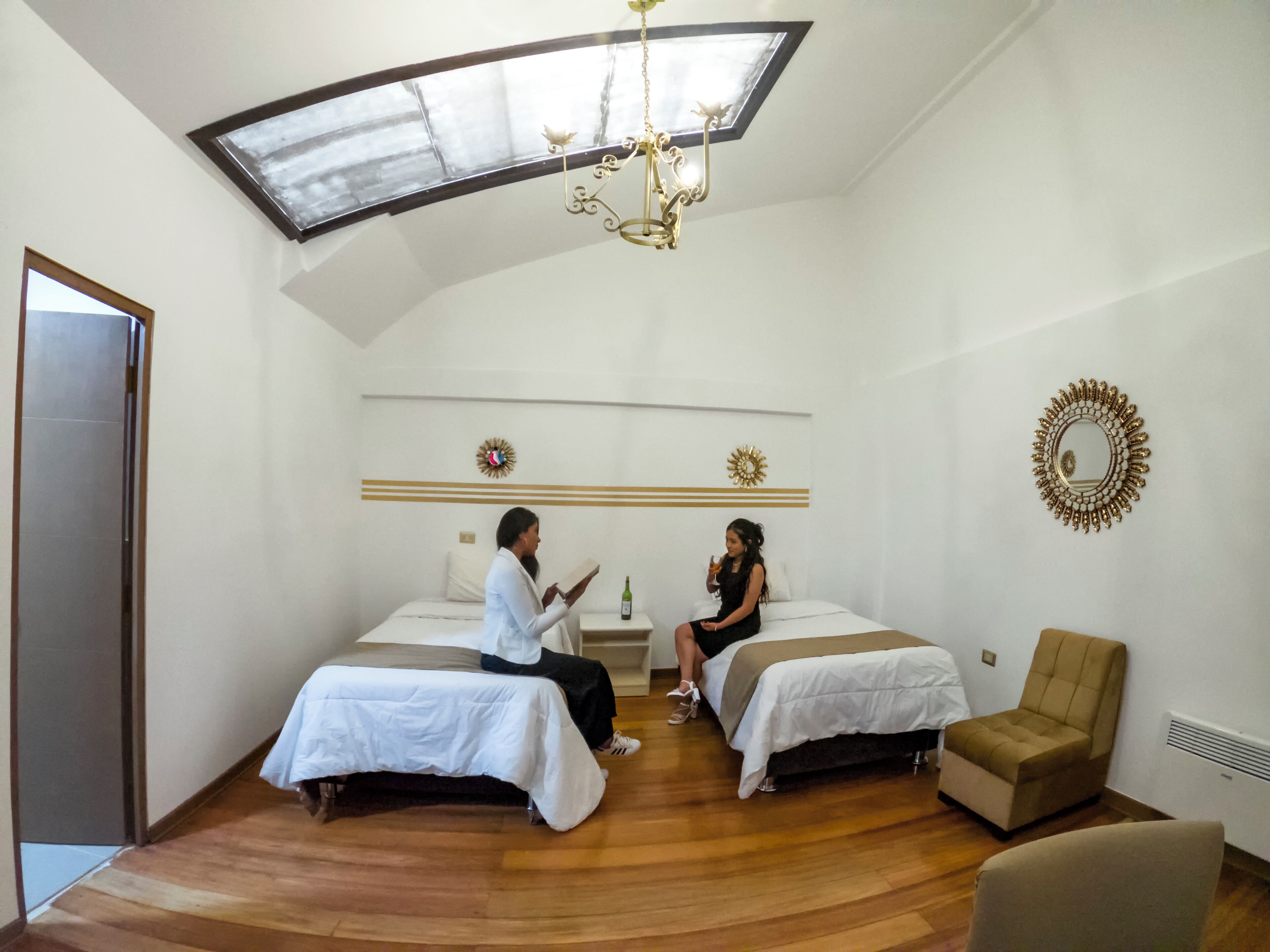 Habitación de hotel con dos camas, un candelabro, un espejo y un sillón pequeño.