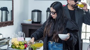 En person som häller upp en dryck i en skål, en kaffebryggare och en fruktskål på ett bord.