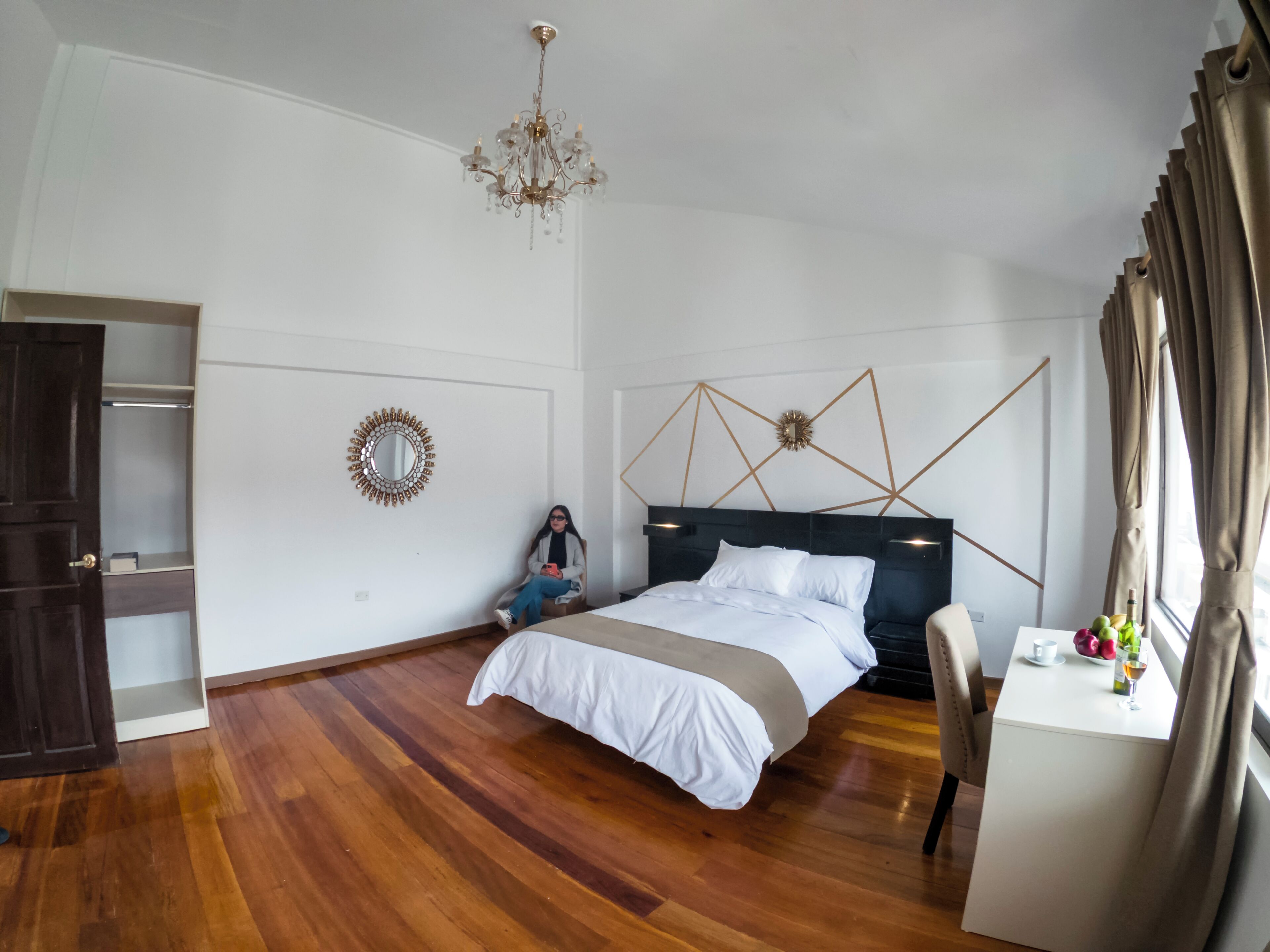 A bedroom with a bed, a chandelier, a mirror, and a desk with a vase of flowers.