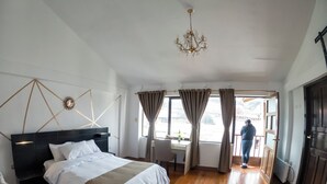 Ett hotellrum med en säng, ett skrivbord, en stol, en kristallkrona och utsikt över omgivningarna.