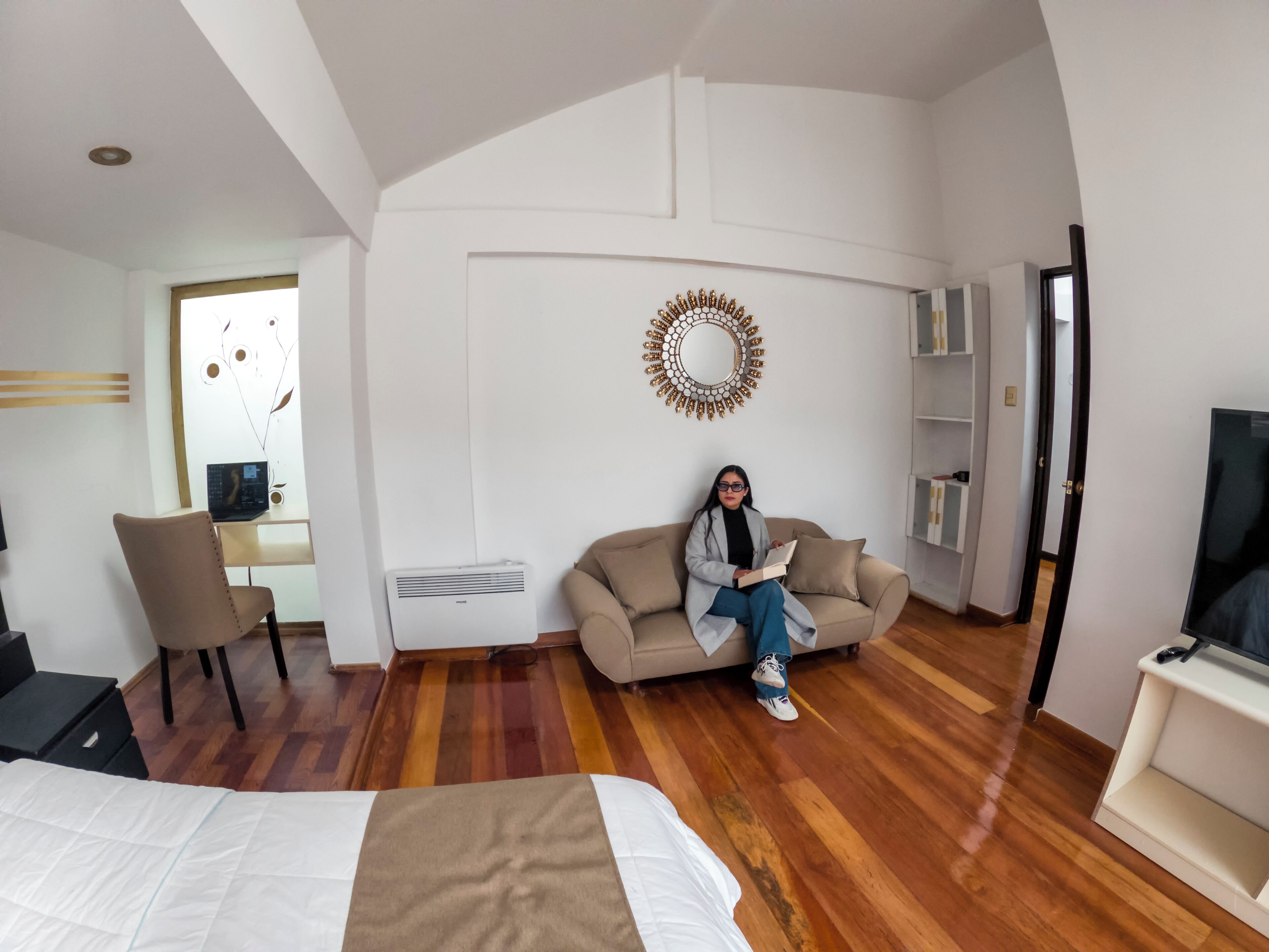 Une chambre d’hôtel moderne équipée d’un lit, d’un canapé, d’un bureau avec un ordinateur portable, d’une télévision et d’un miroir décoratif.