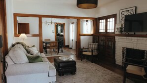 A living room with a sofa, ottoman, fireplace, and a dining area with chairs and a table. - Vintage Style Home Near Downtown | W&D + Patio (Wichita)