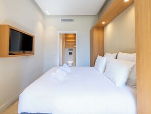 Een hotelkamer met een groot bed, een aan de muur bevestigde televisie en een badkamer door een open deur zichtbaar.
