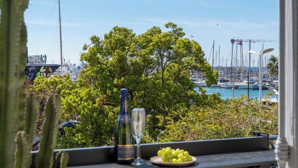 A table with a bottle, a glass, and grapes, overlooking a marina with boats and a bridge. - 2-Br Facing Palais des Congrès – Cannes City Centre (Cannes)