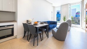 A modern kitchen with a dining area, a blue sofa, and a balcony with a view. - 2-Br Facing Palais des Congrès – Cannes City Centre (Cannes)