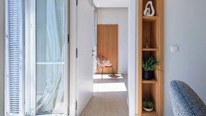 A modern interior with a sliding glass door, a wooden door, a chair, a shelf with plants, and a switch on the wall. - 2-Br Facing Palais des Congrès – Cannes City Centre (Cannes)