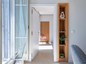 A modern interior with a sliding glass door, a wooden door, a chair, a shelf with plants, and a switch on the wall. - 2-Br Facing Palais des Congrès – Cannes City Centre (Cannes)