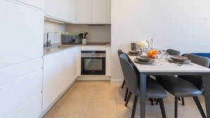 A modern kitchen with white cabinets, a built-in oven, and a dining area with a table set for two. - 2-Br Facing Palais des Congrès – Cannes City Centre (Cannes)
