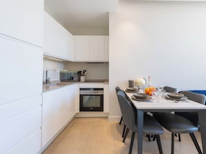 A modern kitchen with white cabinets, a built-in oven, and a dining area with a table set for two. - 2-Br Facing Palais des Congrès – Cannes City Centre (Cannes)