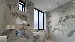 Ein modernes Badezimmer mit Marmorverkleidung, einem integrierten Waschbecken, einer Toilette und einer Badewanne.
