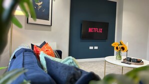 Ein modernes Wohnzimmer mit einer Couch, einem Couchtisch mit einer Sonnenblumenvase und einem an der Wand montierten Fernseher.