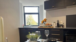A modern kitchen with dark cabinets, a window, and a dining area set for a meal. - Welcome to The Aviary – Upper (Bournemouth)