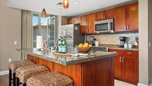 Una cocina moderna con armarios de madera, electrodomésticos de acero inoxidable, una isla grande con asientos e iluminación colgante.
