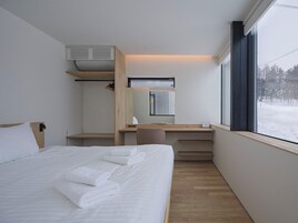 Une chambre d’hôtel moderne équipée d’un lit, d’un bureau, d’une chaise, d’un miroir et d’une fenêtre donnant sur un paysage enneigé.