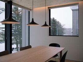 Une salle de conférence dotée d’une grande table, de deux lampes suspendues et offrant une vue sur des arbres couverts de neige, visible à travers une grande fenêtre.