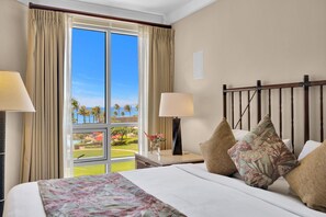 A hotel room with a large window, a bed with floral bedding, two bedside lamps, and a nightstand with a vase of flowers. - KBM Resorts | 4 FREE CARS | Honua Kai Hokulani | Ocean view | 7-Bedroom Multi-Unit Listing Recently Remodeled! HK ML-2939 (Lahaina)