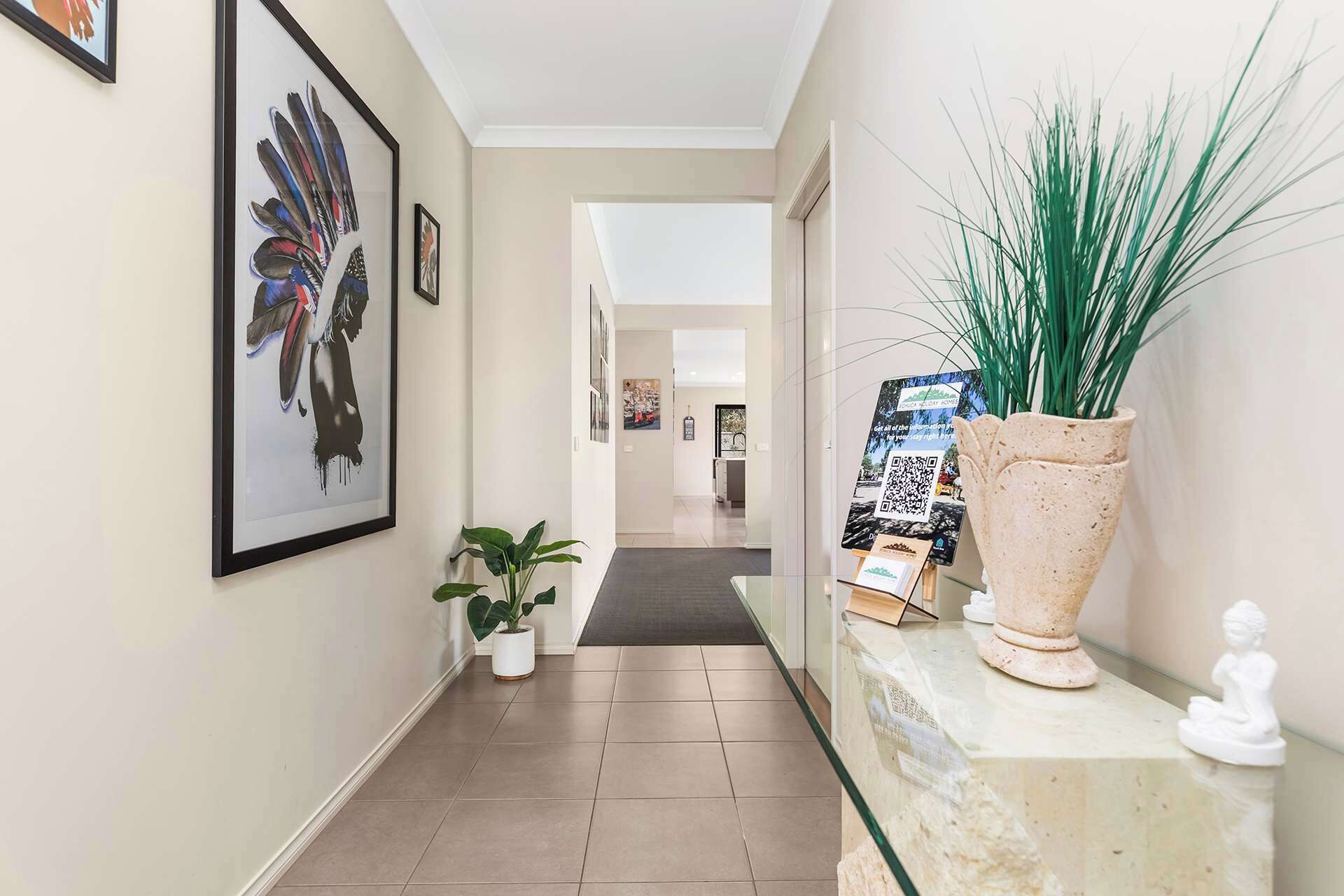 A hallway with framed artwork, a potted plant, a QR code display, and a statue.