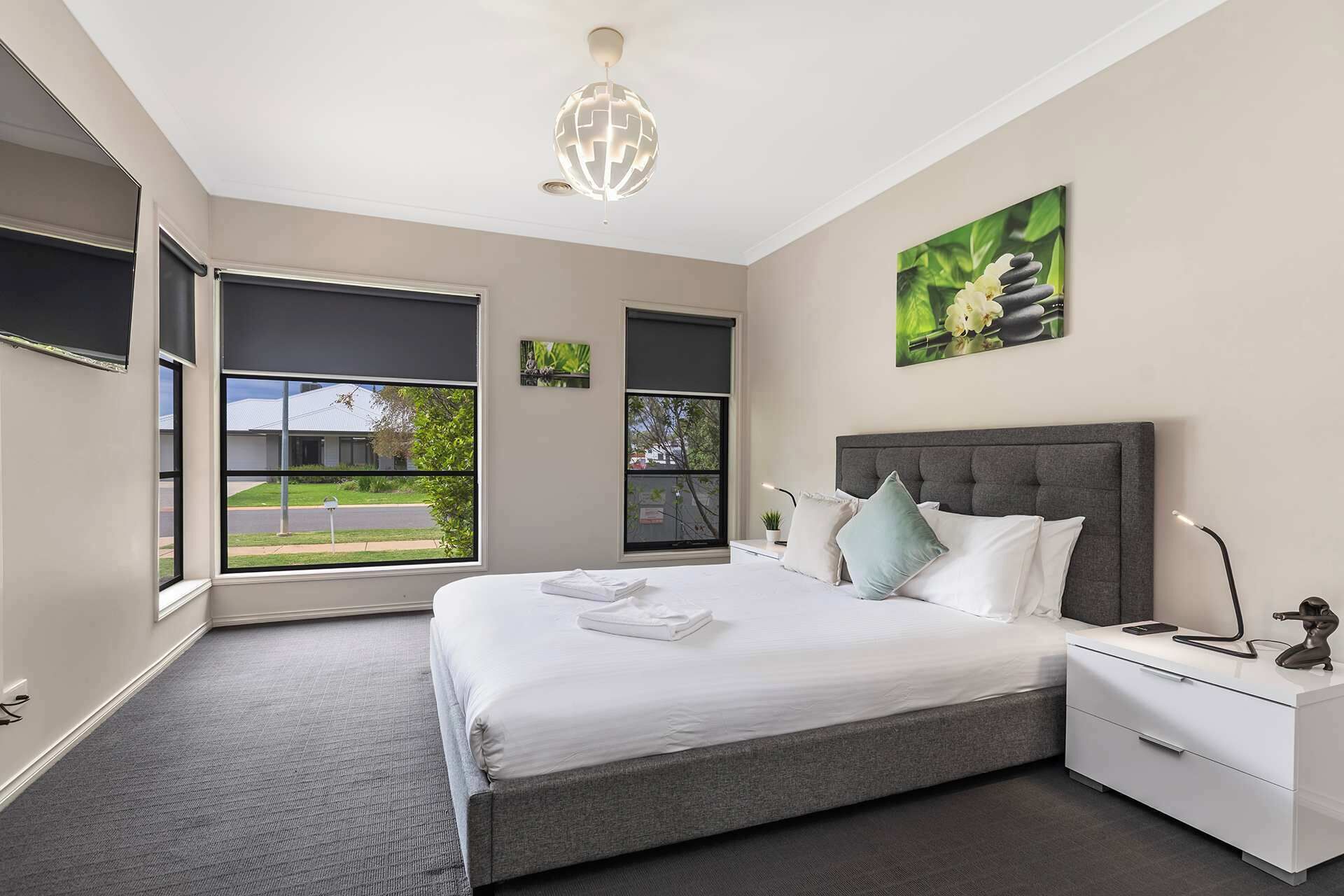 A modern bedroom with a large bed, bedside tables, a nightstand, a globe light, and a view of the outdoors.