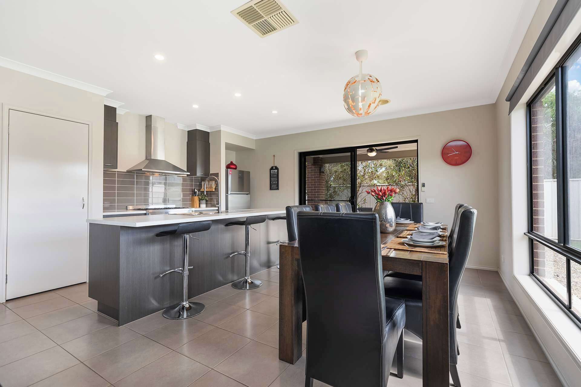 A modern kitchen with a central island, bar stools, and a dining area with a table and chairs.