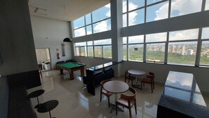 A spacious room with a pool table, billiard cues, and a view of a cityscape through large windows.