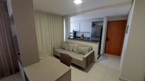 A modern living room with a sofa, a dining table, and a kitchen in the background.