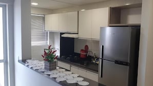 A modern kitchen with stainless steel appliances, a window with blinds, and a decorative plant.